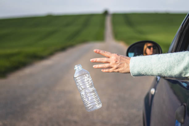 istock Driver throwing away plastic bottle from car window on road. 1145046514