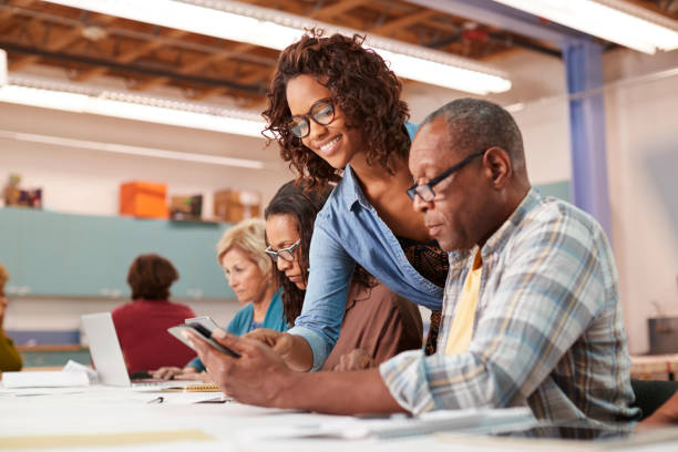 istock Teacher Helping Retired Senior Man Attending IT Class In Community Centre 1145048297