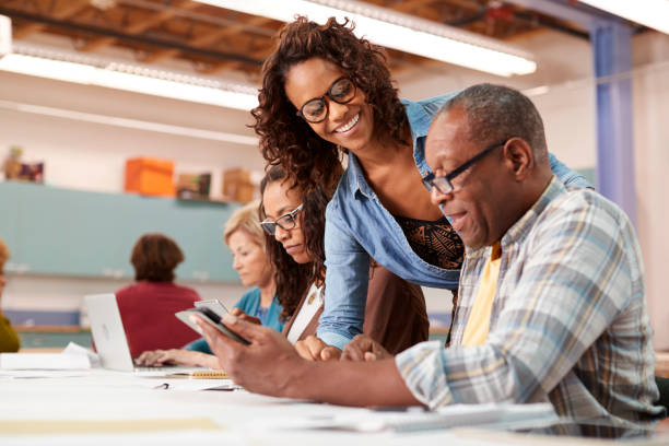 istock Teacher Helping Retired Senior Man Attending IT Class In Community Centre 1145048425