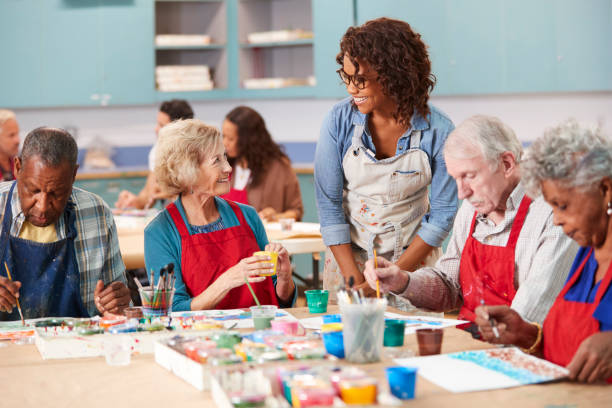 Group Of Retired Seniors Attending Art Class In Community Centre With Teacher Group Of Retired Seniors Attending Art Class In Community Centre With Teacher community center photos stock pictures, royalty-free photos & images