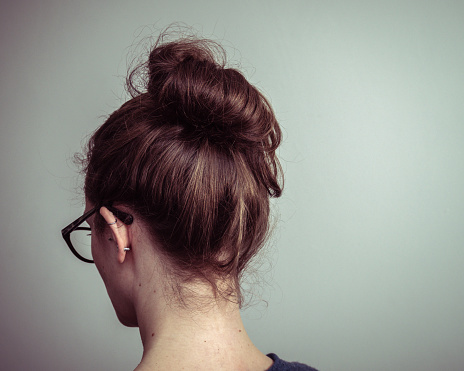 Caucasian woman with glasses, from behind showing brown hair in a ponytail
