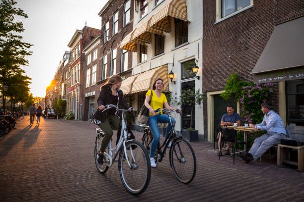 Two young girls ride a bike through the historic center of Leiden, while two men enjoy a snack on the terrace of a bar.