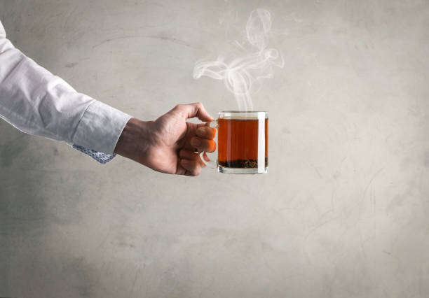 A side lit cup and saucer sit on a glass table, steam is visible rising from the cup.