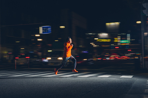 A Japanese man and runner runs through the streets of Tokyo. He is wearing running clothing and speeds through the streets as he loves to stay healthy and in top fitness while in the city. Image taken in Tokyo, Japan.