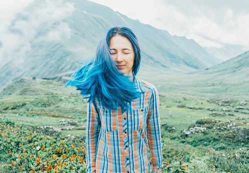 Beautiful young woman with blue hair standing on background of mountains in summer.