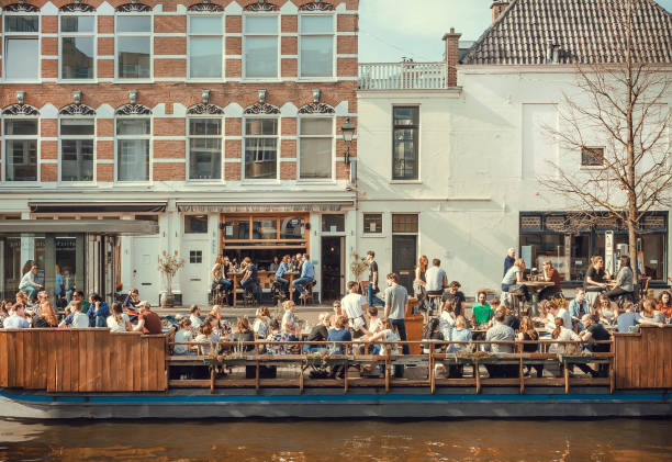 Many people eating and talking on riverboat cafe on the canal in a sunny day stock photo