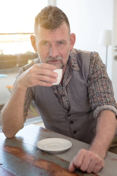 istock handsome man in his 50s sitting at table and drinking coffee 1145060934