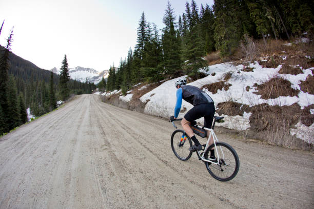 Gravel Road Bicycle Rider A man rides his cyclo-cross bicycle on a remote gravel road in British Columbia, Canada. His bicycle has large tires and is designed to ride on rough terrain. He has three small gear bags strapped to his bicycle. cycling vest photos stock pictures, royalty-free photos & images