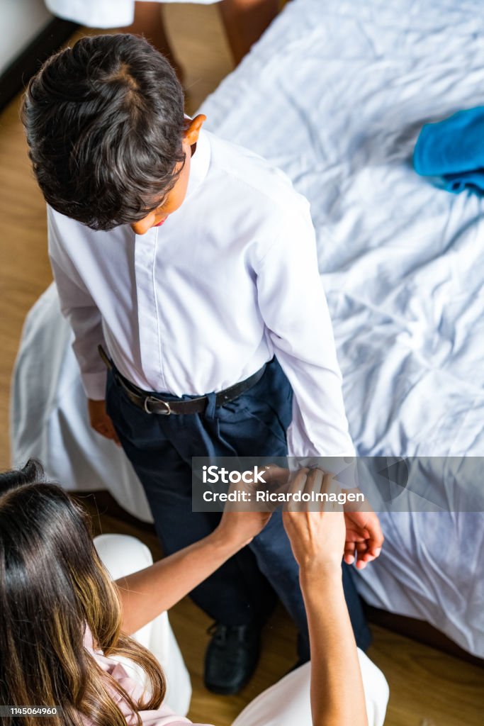 Madre Latina Vistiendo A Su Hijo Para Ir A La Escuela En La Sala De Juegos Foto de stock y más banco de imágenes de Adulto - iStock Madre Latina Vistiendo A Su Hijo Para Ir A La Escuela En La Sala De Juegos Foto de stock y más banco de imágenes de Adulto - iStock