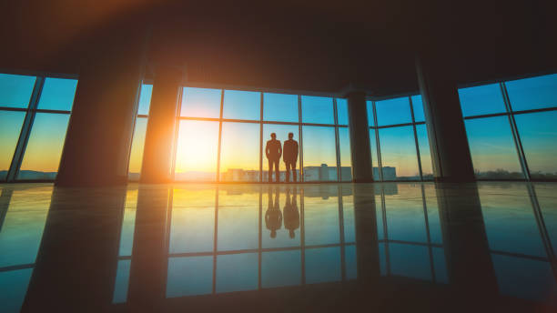 los dos hombres están cerca de la ventana panorámica en el fondo del atardecer - window sun sunlight vertical fotografías e imágenes de stock