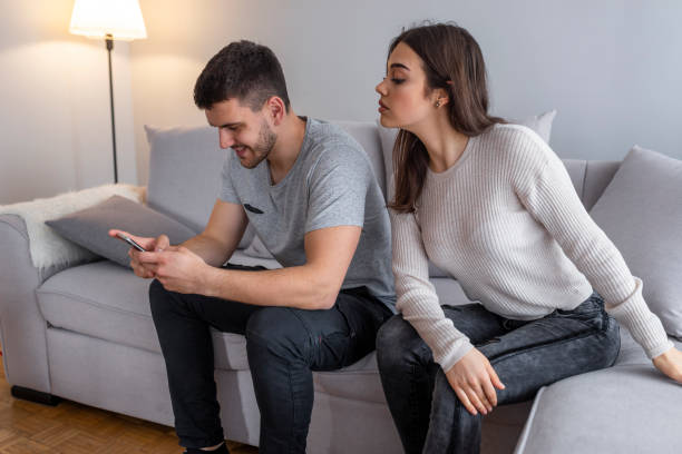 Jealous suspicious mad wife arguing with obsessed husband holding phone texting cheating on cellphone Emotional upset couple sitting on couch and quarreling about smartphone, mistrust concept. Jealous suspicious mad wife arguing with obsessed husband holding phone texting cheating on cellphone suspicious message stock pictures, royalty-free photos & images