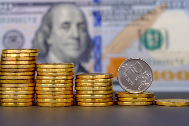 istock Russian ruble in coin rolling down on 100 dollar banknote background. 1145073005