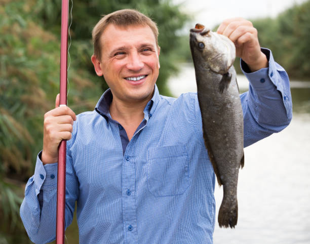 istock Fisherman holding catch freshwater fish in hands on lake 1145076623