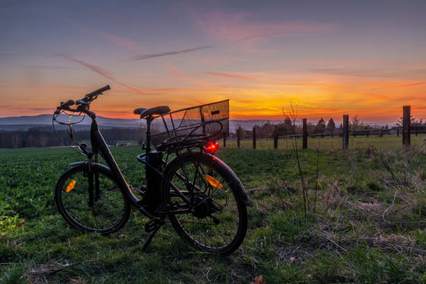 Black electric bicycle with sunset on light green meadow in spring color evening