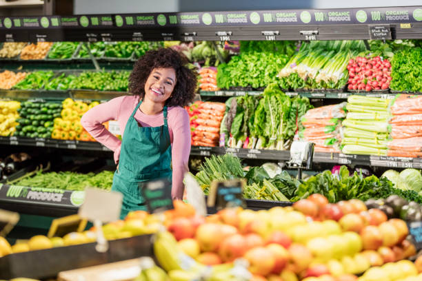 Young African-American woman working in grocery store A young African-American woman in her 20s working in the produce aisle of a grocery store, surround by fresh fruits and vegetables. produce section stock pictures, royalty-free photos & images