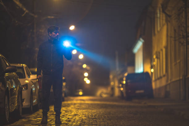 The man with a flashlight stand on the street. Evening night time
