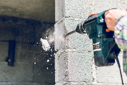 Construction industry worker using pneumatic hammer drill to cut the wall concrete brick, close up