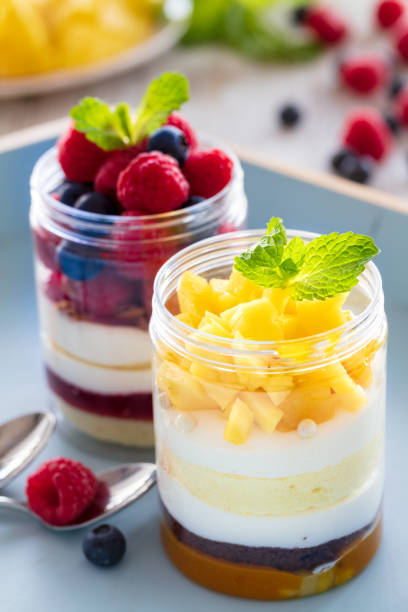 Raspberry and mango dessert, cheesecake, trifle, mouse in a glass jar on a light wooden background, vertical composition stock photo