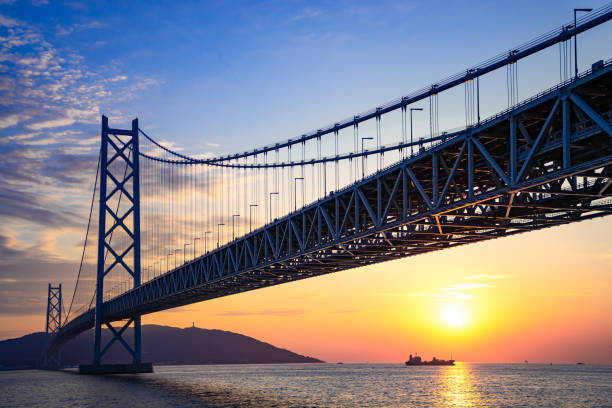 большой мост, сияющий на заходящее солнце - kobe bridge japan suspension bridge стоковые фото и изображения