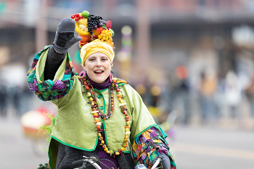 St. Louis, Missouri, USA - March 2, 2019: Bud Light Grand Parade, Woman wearing a friut hat riding a bicycle down 7th street during the parade