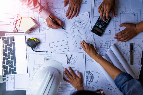 istock engineers pointing to building on blueprint and using laptop to drawing design building Project in office, construction concept. Engineer concept 1145141539