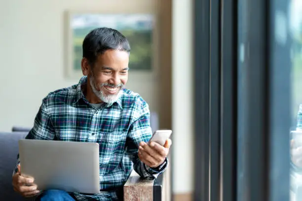 Photo of Candid of old asian retired man using mobile phone to transfer money online or financial payment and read text, smile or laugh with happy and positive. Senior asian with digital technology concept.