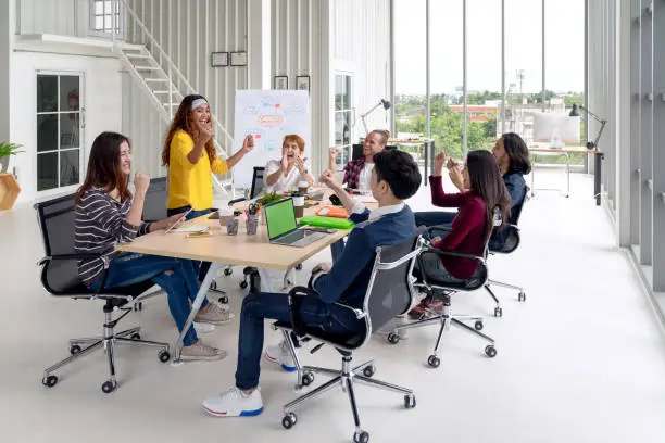 Photo of Group of young attractive asian creative design team meeting at office celebrating success or winner. Asian employee engaged together with effective and productive meeting and happy workplace concept.