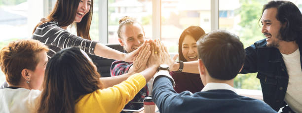 gesto mano alta cinco de grupo empleado riendo junto con la misión de achivement en la compañía millenial. negocio casual con amigos en el trabajo en equipo celebración de la comunidad, ganar y conquista concepto - cheering business people group of people fotografías e imágenes de stock