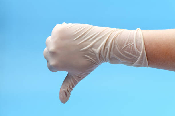 Fragment of a hand in white medical gloves that shows thumb down on a blue background. Show thumb down. Medical background Fragment of a hand in white medical gloves that shows thumb down on a blue background. Show thumb down. Medical background sign human hand pointing manual worker stock pictures, royalty-free photos & images