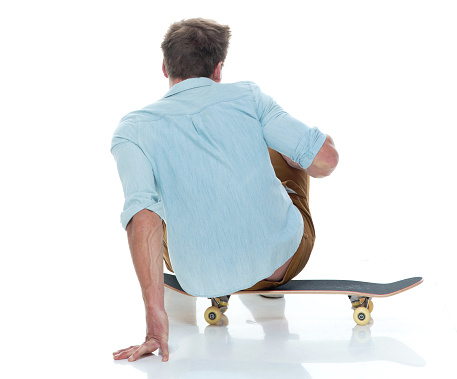 Casual well dressed man sitting on a skateboard