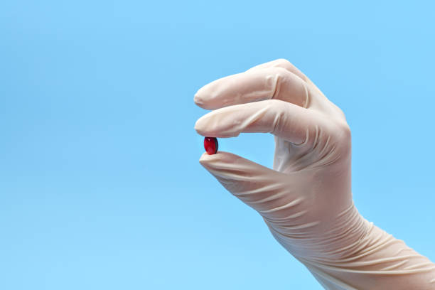 close-up de un fragmento de mano en un guante médico blanco sosteniendo una píldora, cápsula sobre un fondo azul. antecedentes médicos - artificial true exam blue fotografías e imágenes de stock