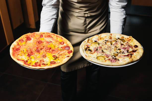 serveur transportant deux assiettes différentes avec une pizza savoureuse. photo avec deux pizzas. pizza aux champignons et pizza au salami. cuisine italienne. restaurant italien. - pizza pizzeria restaurant waiter photos et images de collection