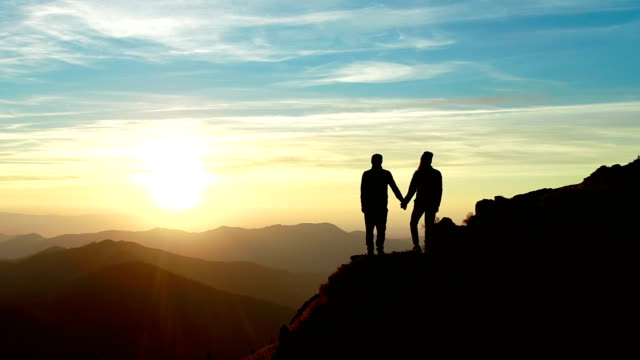The couple standing on the mountain and watching to a beautiful sunrise