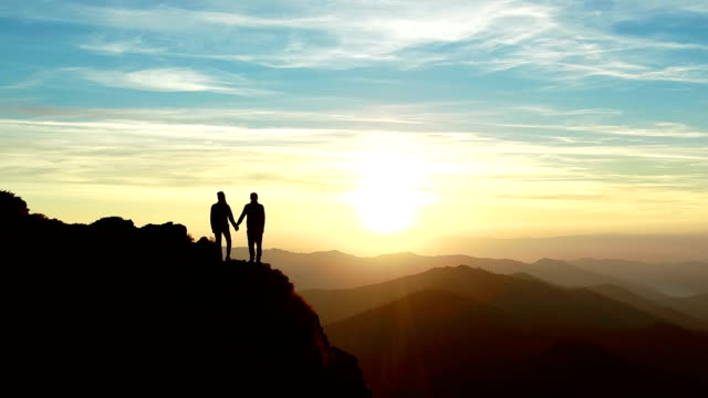 The man and a woman standing on the mountain and watching to a beautiful sunrise