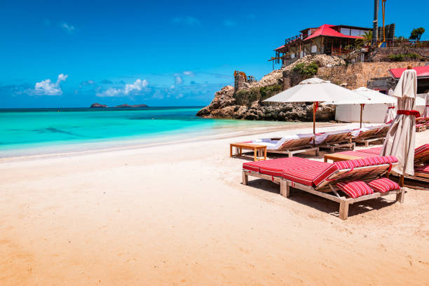 Luxury beach chairs and umbrella on exotic beach in St Barths, Caribbean Island. Idyllic white sandy beach, turquoise calm sea and blue sky. Luxury beach chairs with umbrella on the side of the image. Colorful landscape of St Jean beach in Saint Barthelemy, St Barts. st jean saint barthelemy stock pictures, royalty-free photos & images