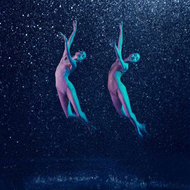 Birds. Two young female ballet dancers under water drops and spray. Caucasian and asian models dancing together in neon lights. Ballet and contemporary choreography concept. Creative art photo.