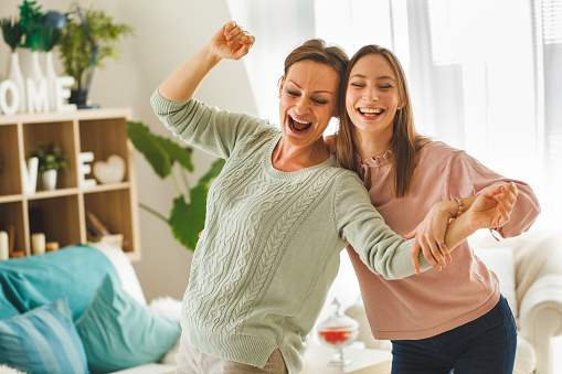Cheerful mother and daughter having fun while dancing together around their living room.