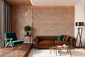 Modern living room interior with brick wall blank wall, leather brown sofa, green lounge chair, table, wooden wall and floor, plants, carpet, hidden lighting. 3d render illustration mockup.