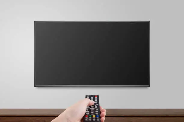 Photo of Television on white wall with hand using remote control, TV 4K flat screen lcd or oled, plasma realistic illustration, Black blank HD monitor mockup.