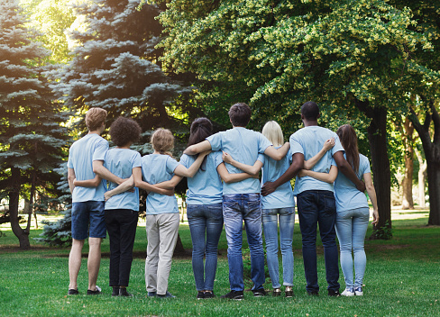 Volunteering, people and ecology concept. Group of volunteers embracing in park, back view, copy space