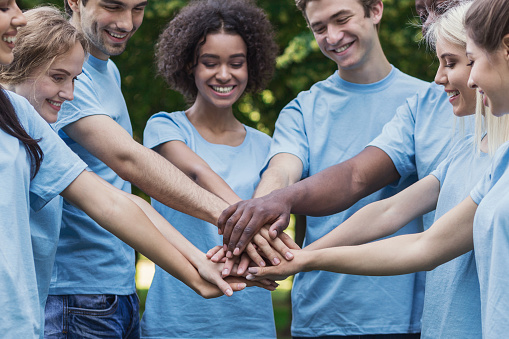 Group of active environmentalists stacking hands in park, greeting power teamwork, copy space