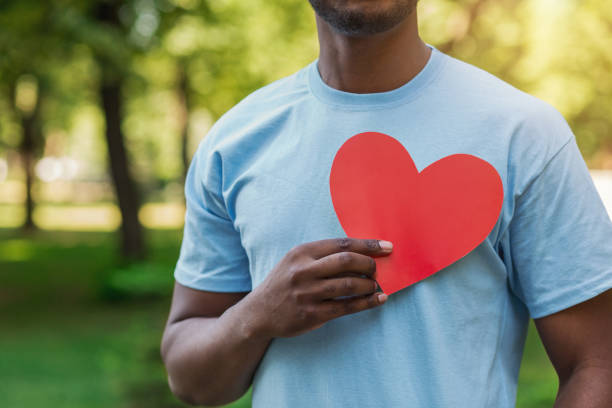 Black man holding red heart on his chest Love, volunteering and charity concept, copy space. Young black man holding red heart on his chest. altruism photos stock pictures, royalty-free photos & images