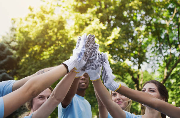 Group of volunteers making high five in park Volunteering, unity and environment care concept. Group of young volunteers in protective gloves making high five before cleaning park, closeup altruism stock pictures, royalty-free photos & images