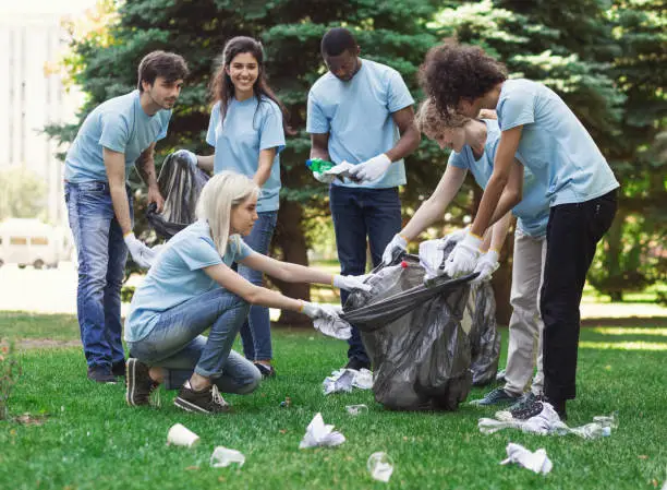 Young volunteers collecting garbage in park, ecology concept, copy space