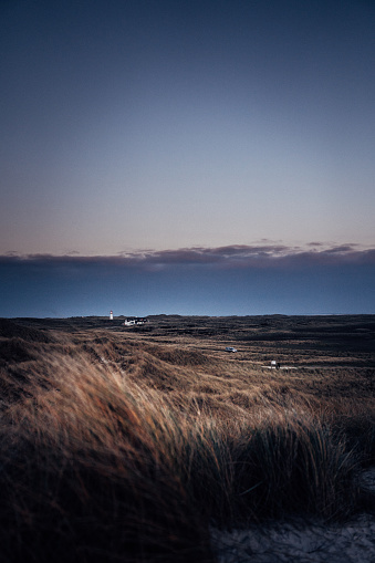 A lighthouse between gras dunes on a cold island after sunset