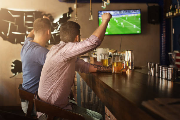 dois amigos que prestam atenção ao jogo de futebol e à cerveja bebendo - beer bar counter bar beer glass - fotografias e filmes do acervo