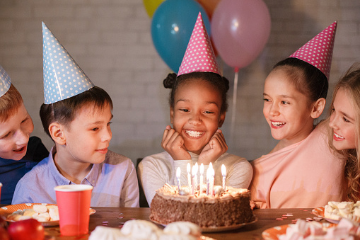 African-american girl looking at birthday cake, having party with friends