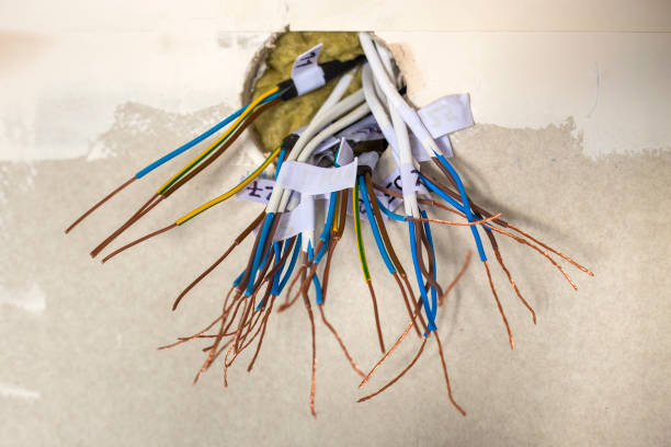 istock Electrical exposed connected wires protruding from socket on white wall. Electrical wiring installation. Finishing works in renovated apartment. 1145195730