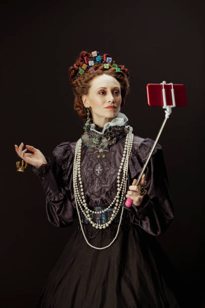 Selfie Queen A modern take on Queen Elizabeth I. The woman portraying her is dressed traditionally but instead of a crown, she has small images of app icons scattered in her hair. She is holding a selfie stick with a phone attached, taking a picture of herself. elizabeth i of england photos stock pictures, royalty-free photos & images