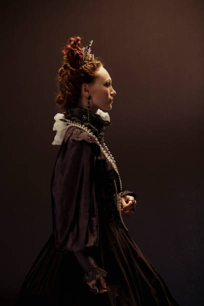 Sideways Antique Portrait Queen Elizabeth I concept. The woman portraying her is dressed traditionally, smiling at the camera in front of a back studio background with her hands in her pockets providing a modern twist. neck ruff stock pictures, royalty-free photos & images